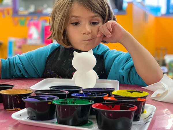 A pre-school child considering what colour to paint a porcelain cat